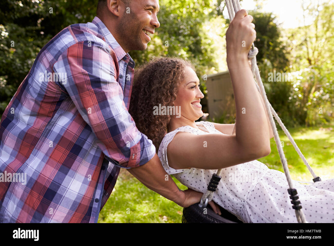 Seitenansicht der Mann schob Frau auf Reifenschaukel im Garten Stockfoto