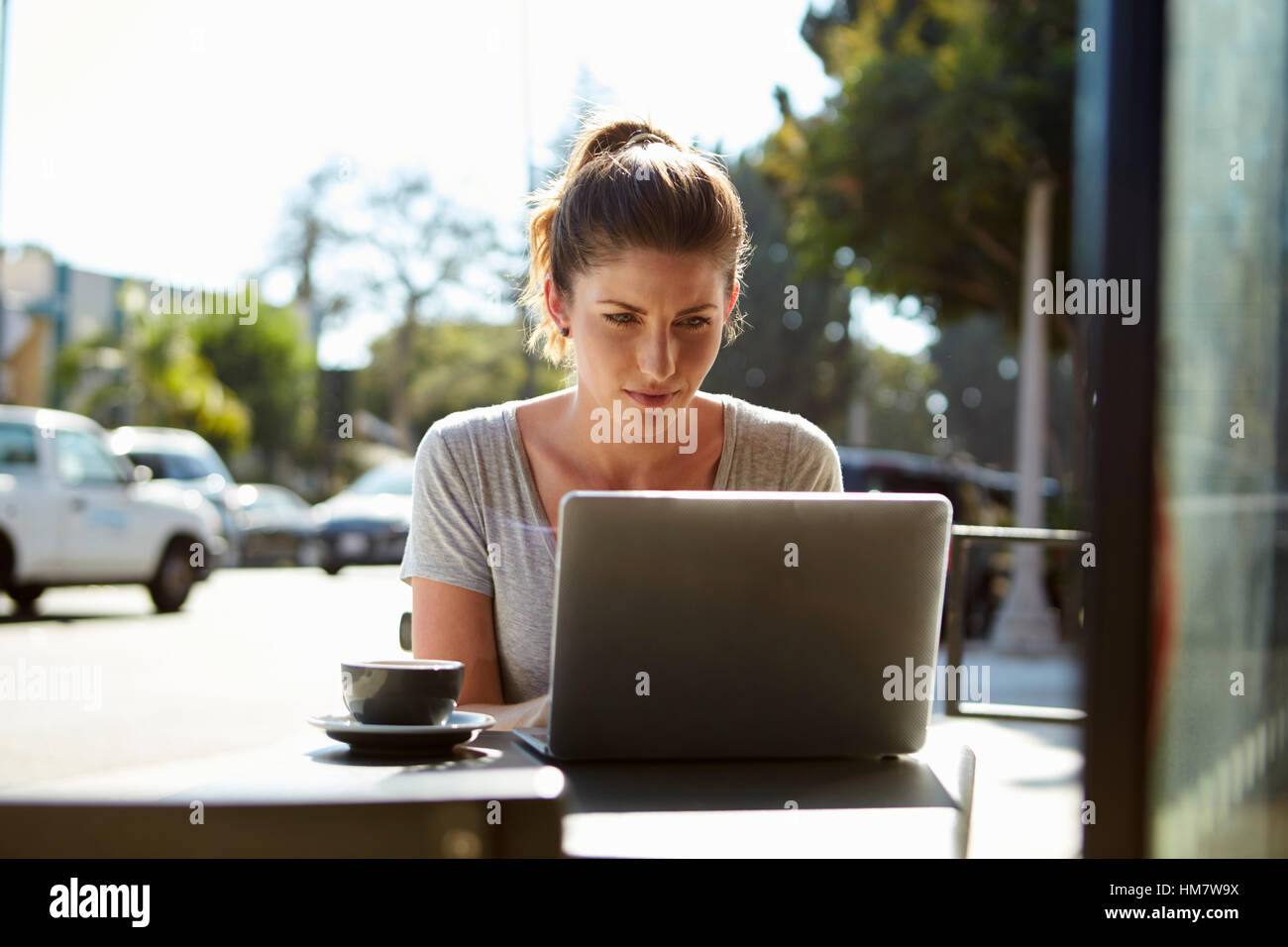 Junge Frau mit Haaren in einem Brötchen mit einem Laptop vor einem café Stockfoto