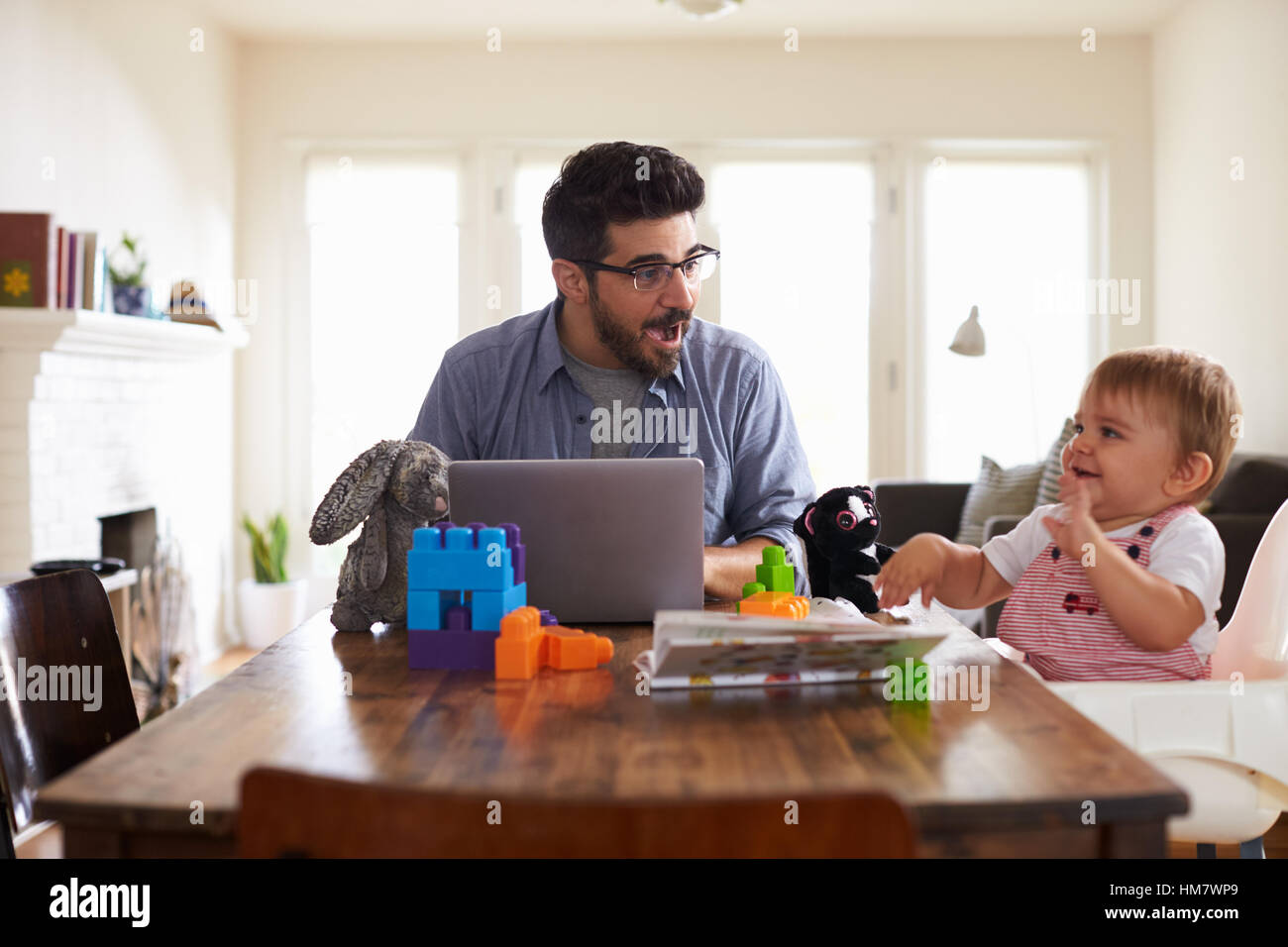 Vater arbeitet auf Laptop wie Baby Sohn spielt mit Spielzeug Stockfoto