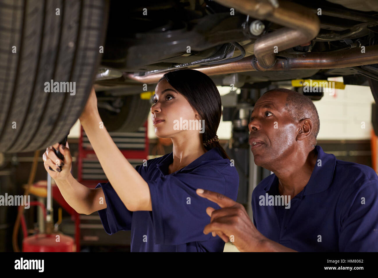 Mechaniker und weiblichen Auszubildenden gemeinsam unter Auto Stockfoto