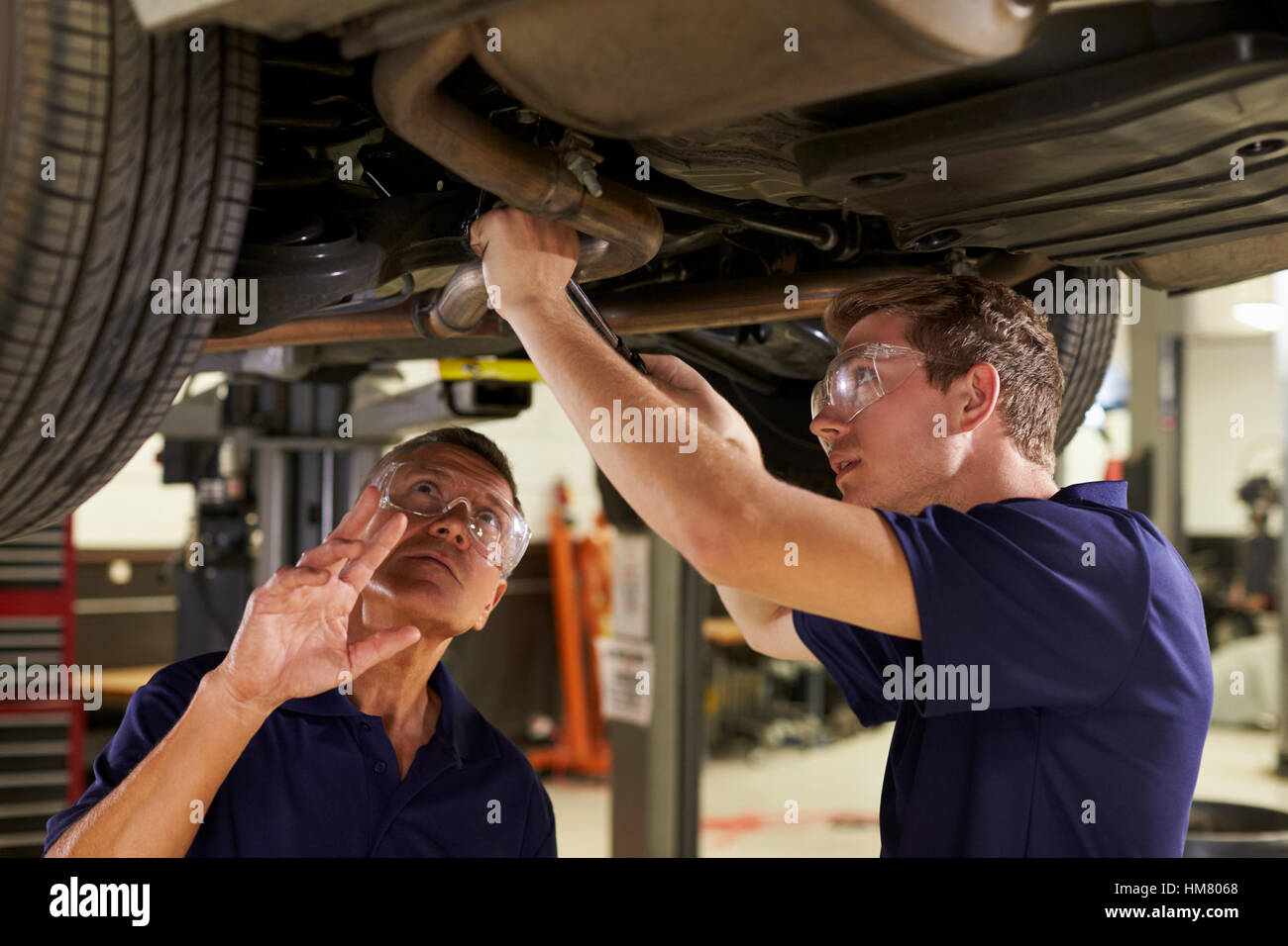 Mechaniker und männlichen Auszubildenden gemeinsam unter Auto Stockfoto