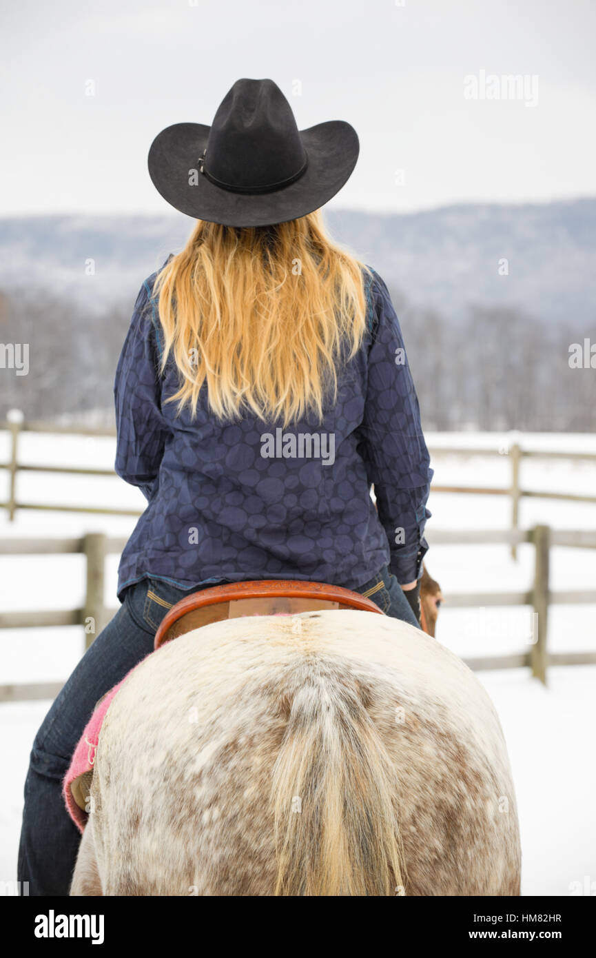 Blonde Frau auf einem grauen Appaloosa Pferd im Winter, junges Cowgirl im westlichen Freizeitkleidung, schwarzer Cowboy-Hut, Jeans Stockfoto