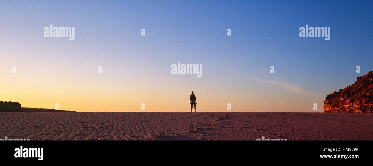 Die Silhouette eines Mannes allein stehend an einem einsamen Strand bei Sonnenuntergang. Stockfoto