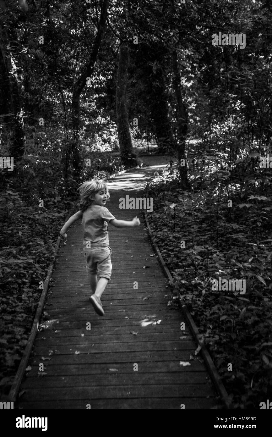 Rückansicht des kleinen Jungen, die entlang der Promenade in Wäldern Stockfoto