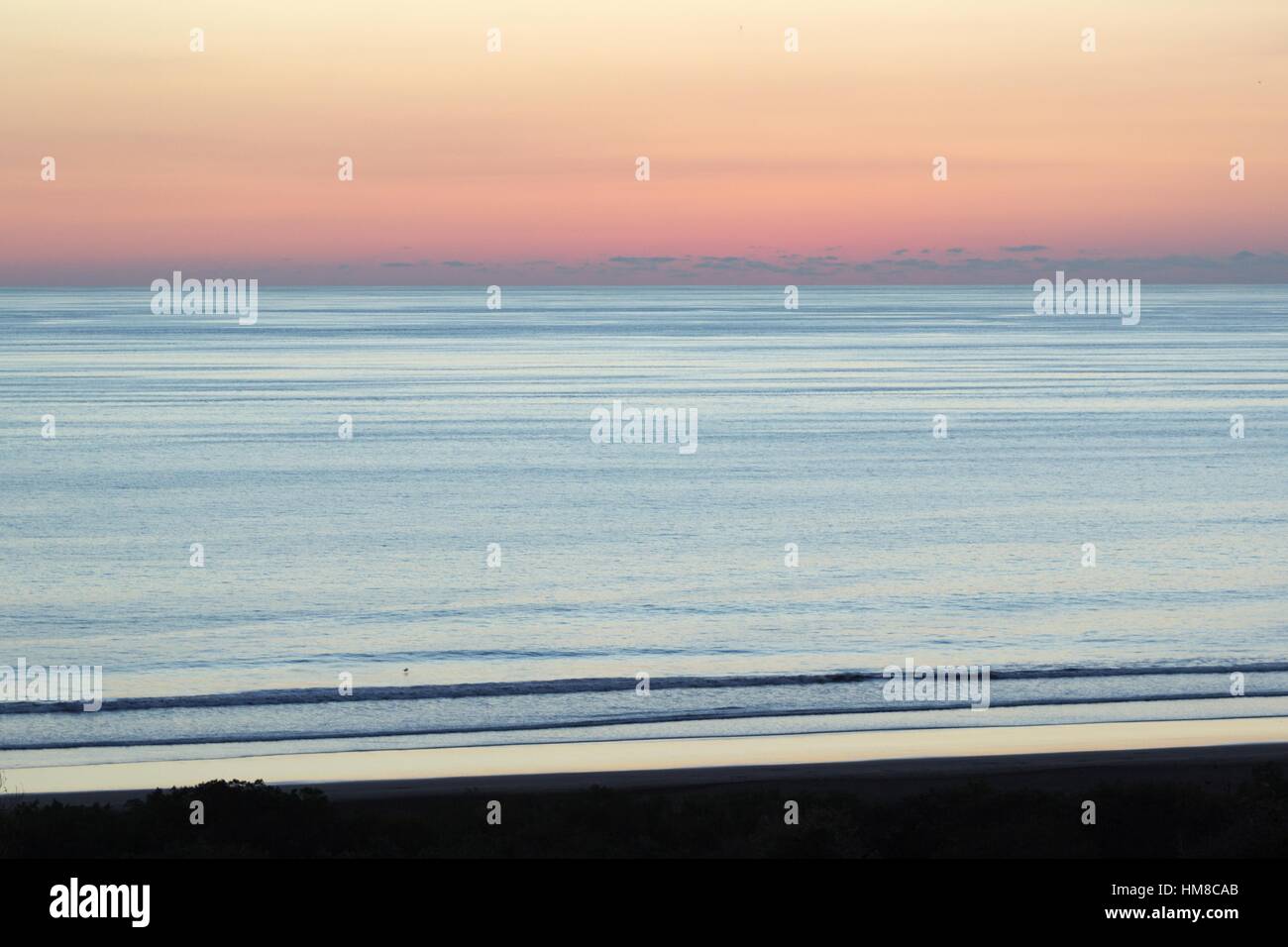 Die Sonne hat nur sank von Blick über dem Pazifischen Ozean und am Himmel leuchtet mit rosa, lila und orange Farbtöne als Brandung gegen das Ufer. Stockfoto