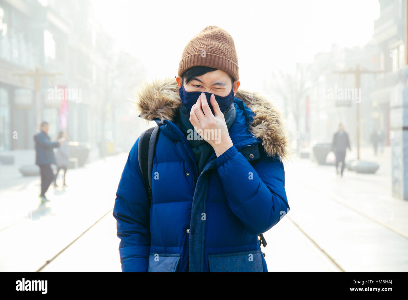 Asiatischen Mann zu Fuß und tragen eine Gesichtsmaske in einem nebligen Smog und dunstigen Tag, wie er leidet unter starken Luftverschmutzung in Peking, China Stockfoto