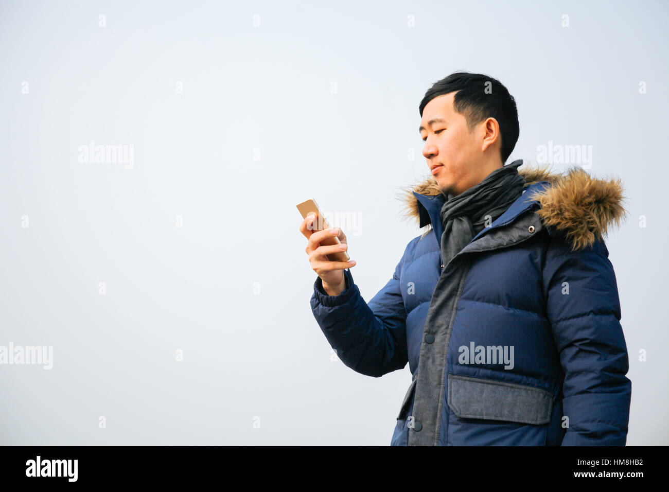 Asiatischer Mann Winterjacke tragen und verwenden ein smart Phone über blauen Himmel Stockfoto