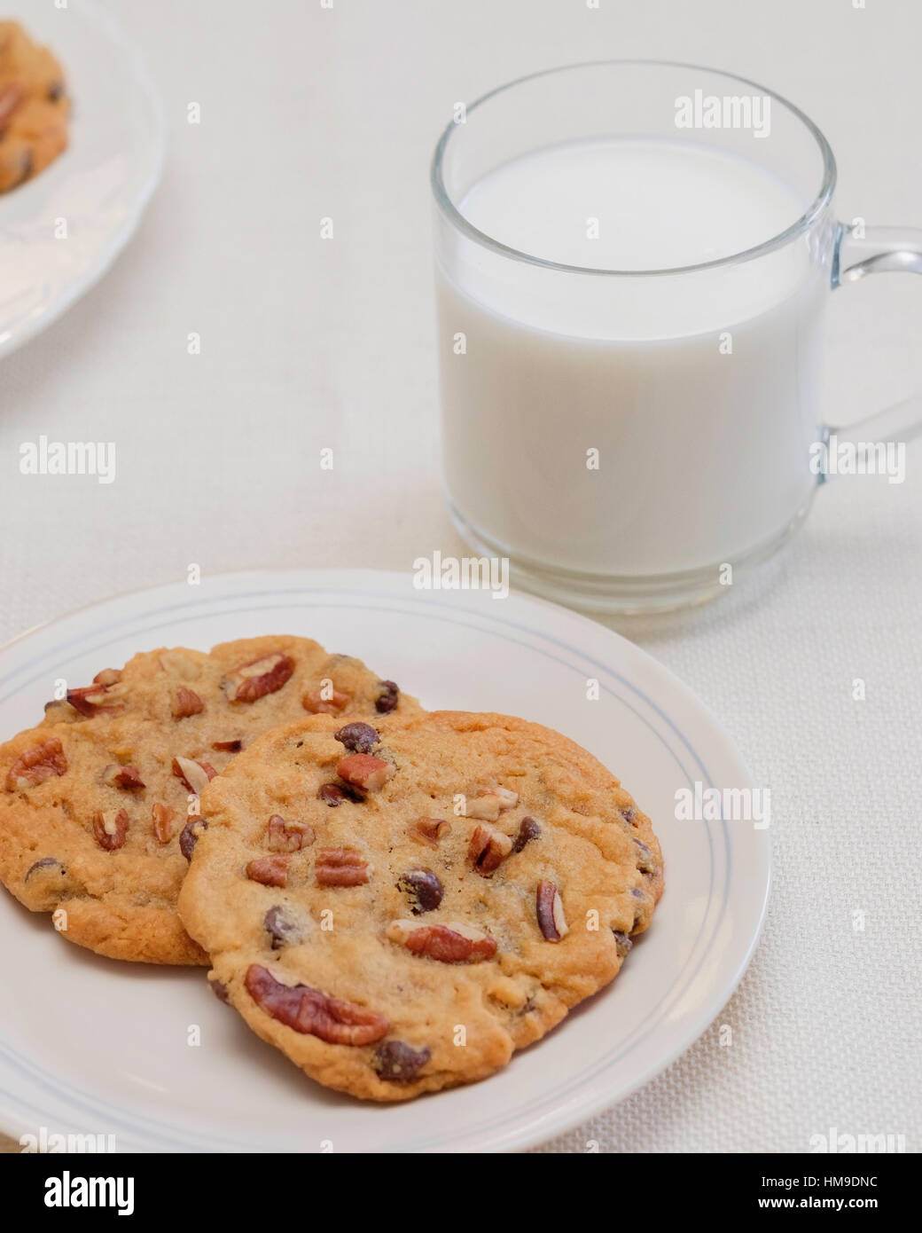 Zwei warme, frische Pecan Schokoladenkekse auf eine Untertasse mit einer Tasse Milch. im Innenbereich. USA. Stockfoto