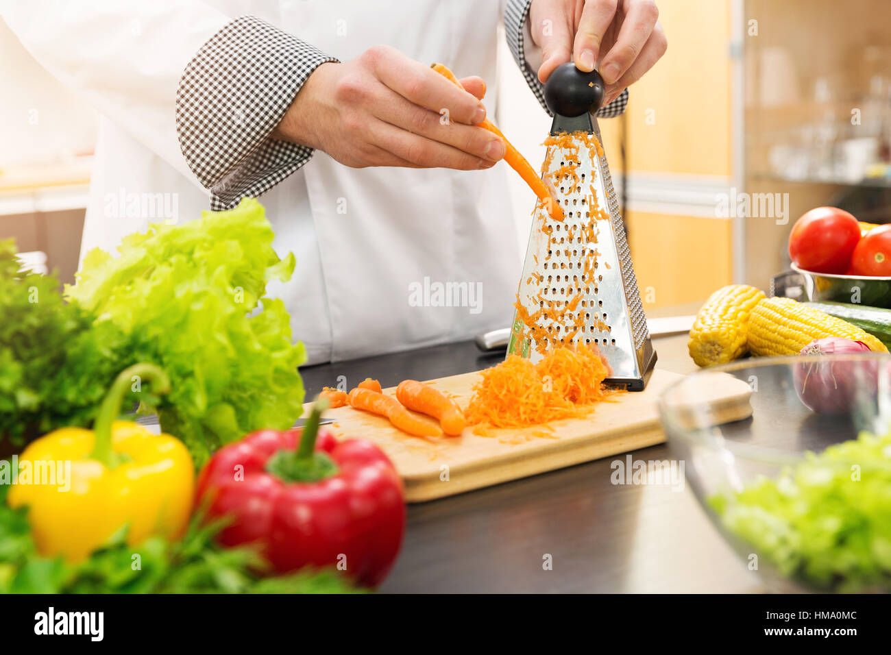 Chef zerkleinern Karotten mit Reibe in Küche Stockfoto