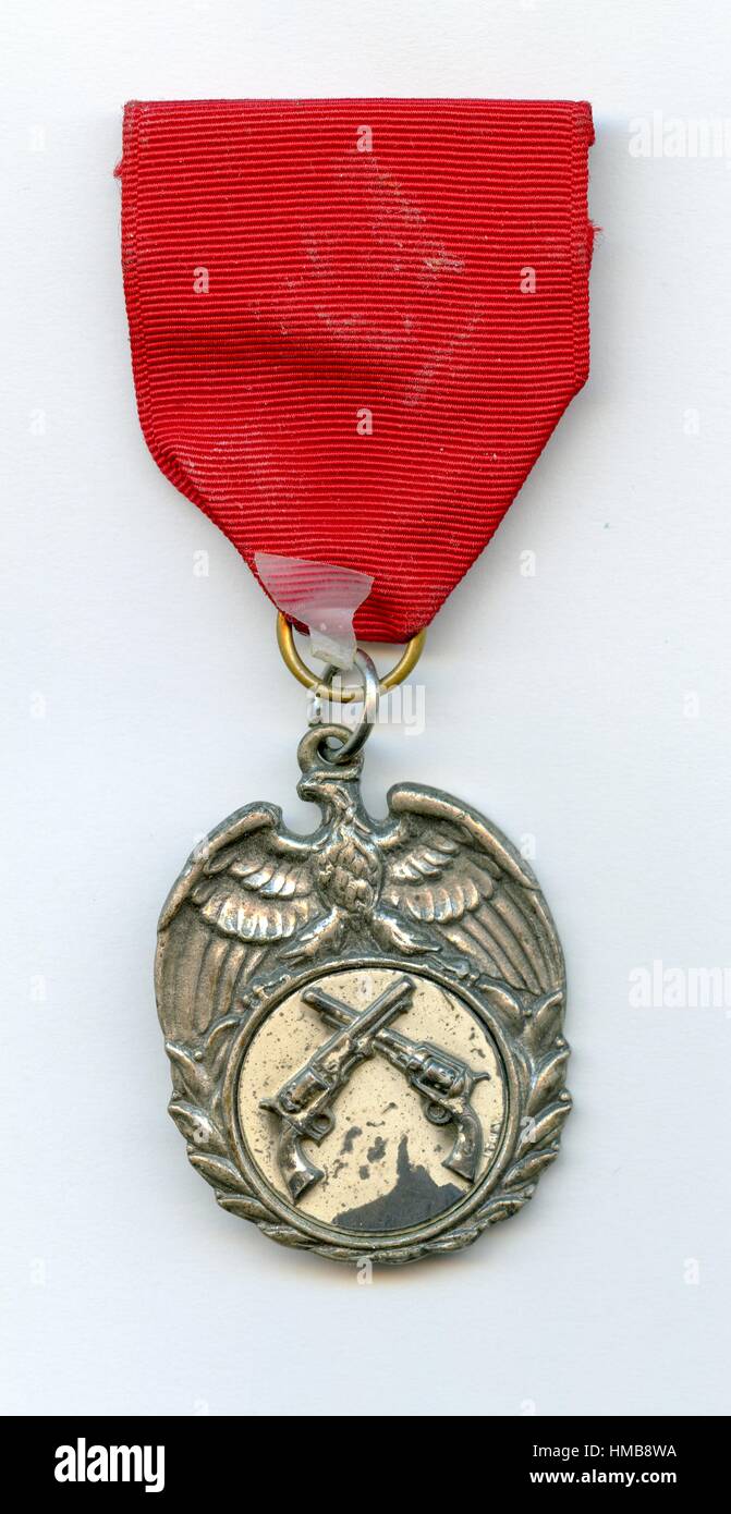 Medaille mit Gerät, bestehend aus zwei gekreuzten Pistolen unter einer Gravur eines Adlers, eine rote Schleife drapieren, möglicherweise als Teil einer Schießwettbewerb, 1950 gegeben über ein integraler und Sprung Ring befestigt. Stockfoto