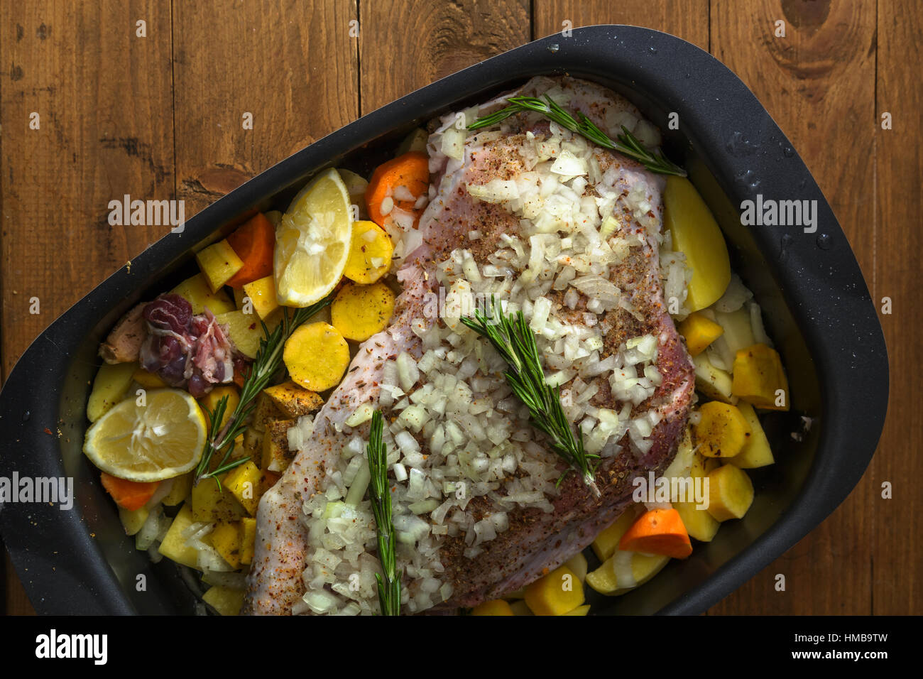 Rohe Lammkeule mit Wurzeln und Zwiebeln zum Braten auf einem rustikalen Holzbrett bereit. Ansicht von oben Stockfoto