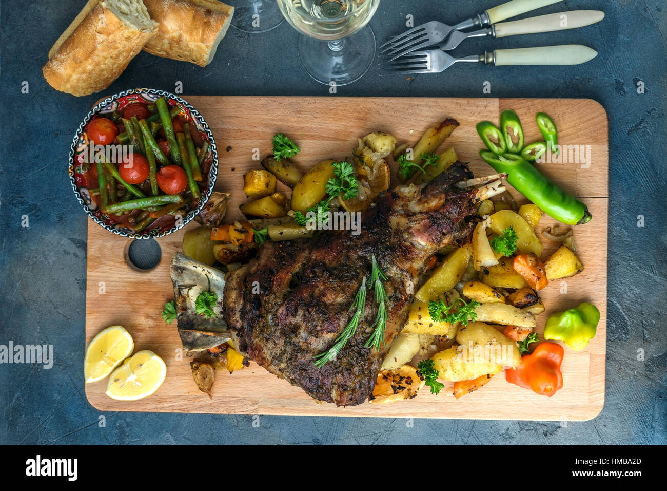 Gebratene Lammkeule mit gerösteten Kartoffeln und Karotten in einem rustikalen Holzbrett, Ansicht von oben gestylt Stockfoto