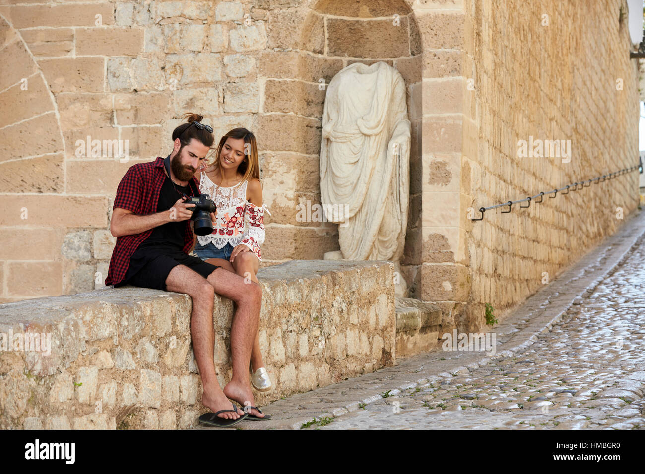 Paar sitzt an Wand betrachten von Fotos auf einer Kamera, Ibiza Stockfoto
