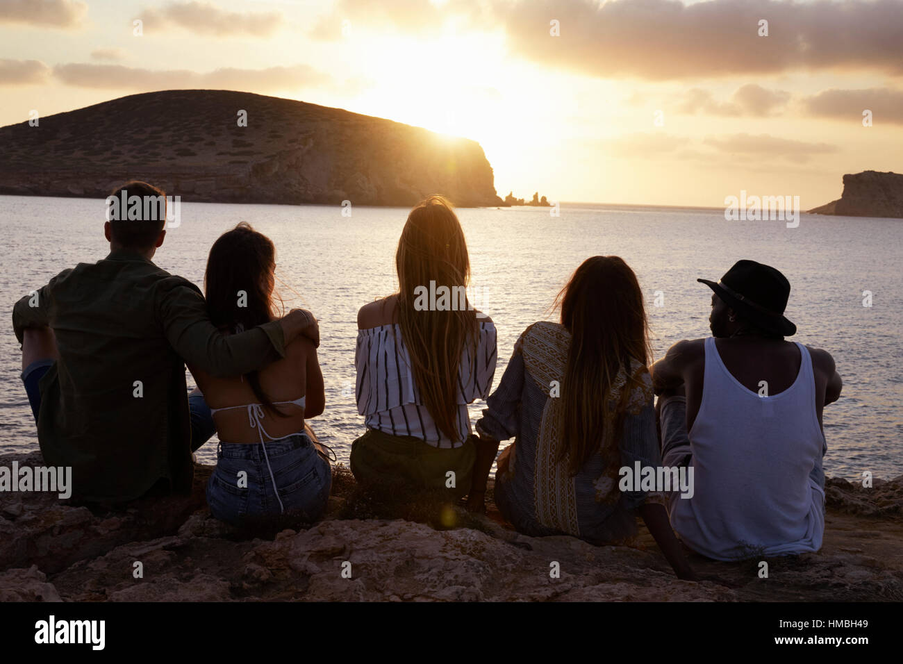 Rückansicht des Freunde sitzen auf Klippe, Sonnenuntergang Stockfoto