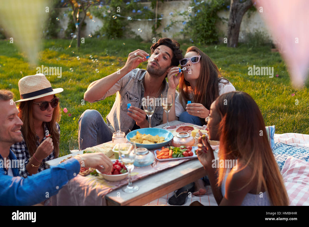 Freunde, die Seifenblasen beim Picknick im Garten Stockfoto