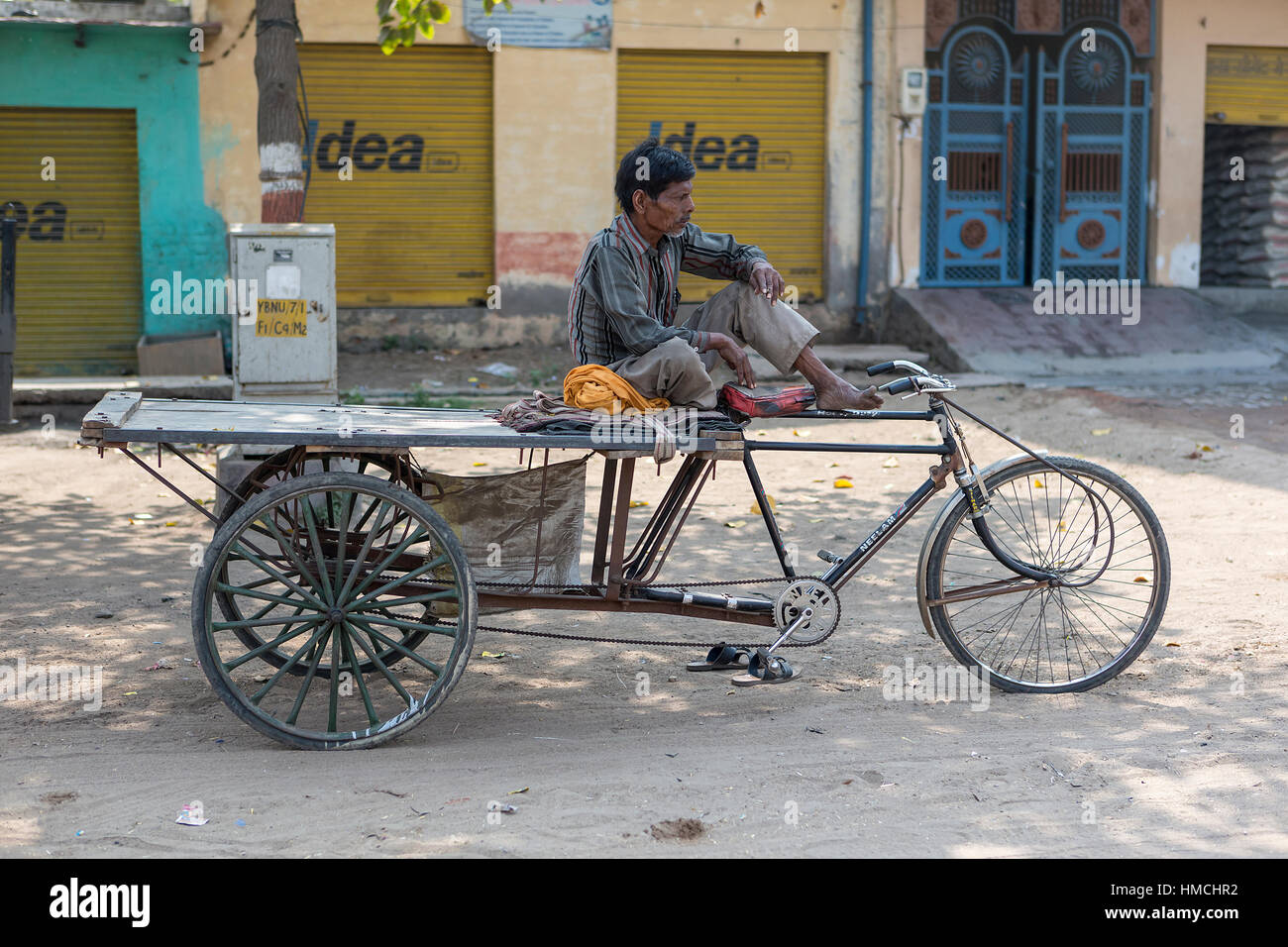 Indischer Mann sitzt im Schatten auf seinem Dreirad entlang der MH92 wartet eine Last zu tragen Stockfoto