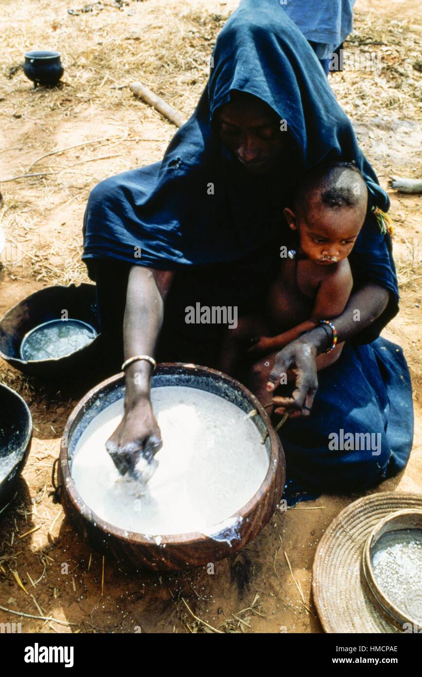 Fulbe-Frau mit einem Kind auf dem Schoß mit Joghurt, Hombori, Mali Hirse-Mehl mischen. Stockfoto