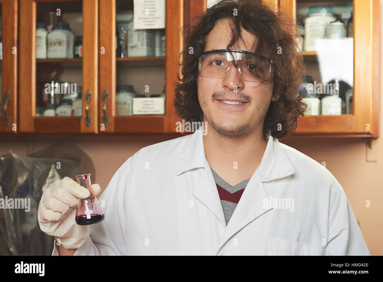 junge lächelnde Chemiker in Googles Besitz purpurrote Flüssigkeit Stockfoto