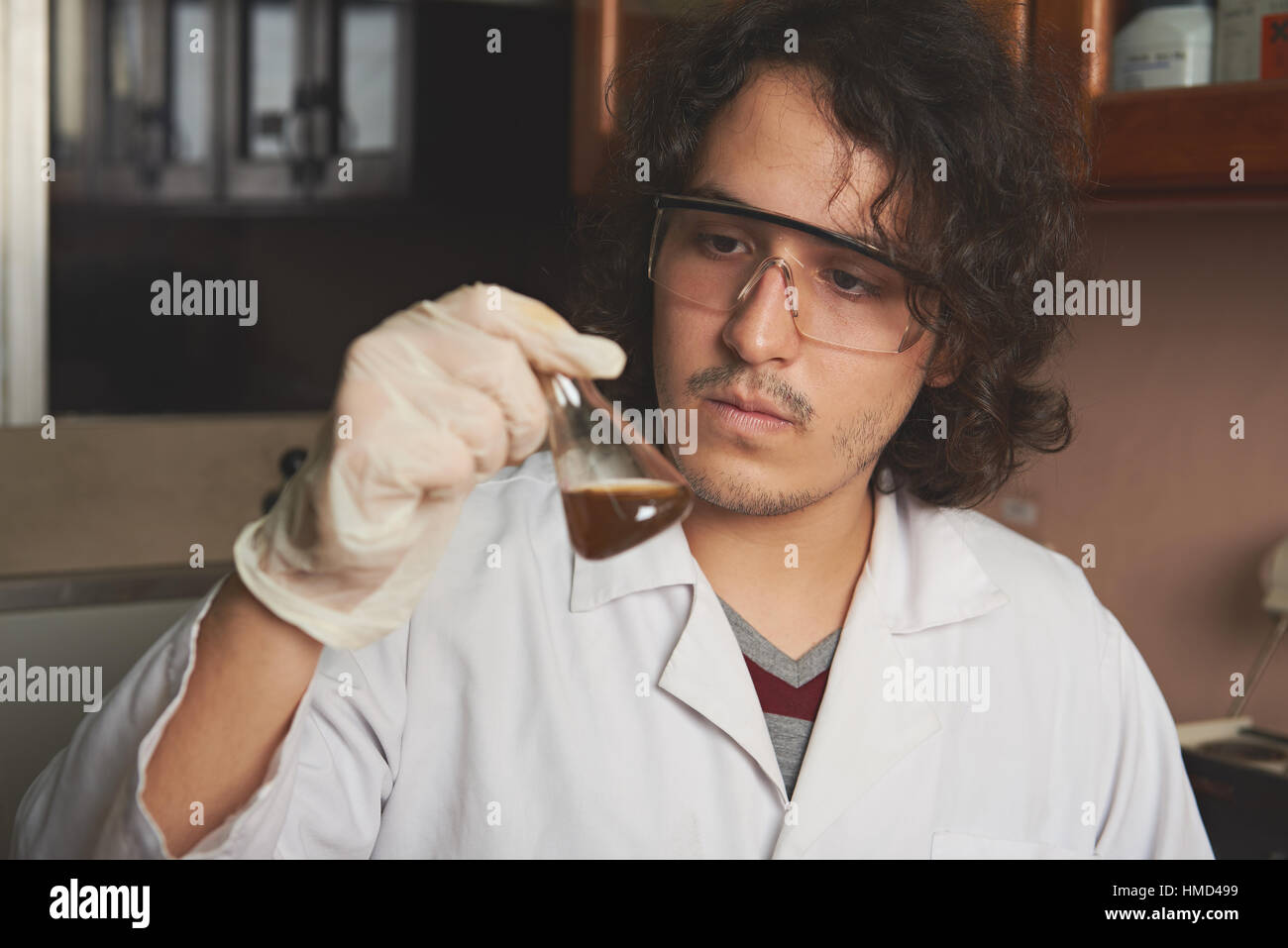 Nachwuchswissenschaftler Mann in Handschuhe halten braune Wasser im Labor Stockfoto