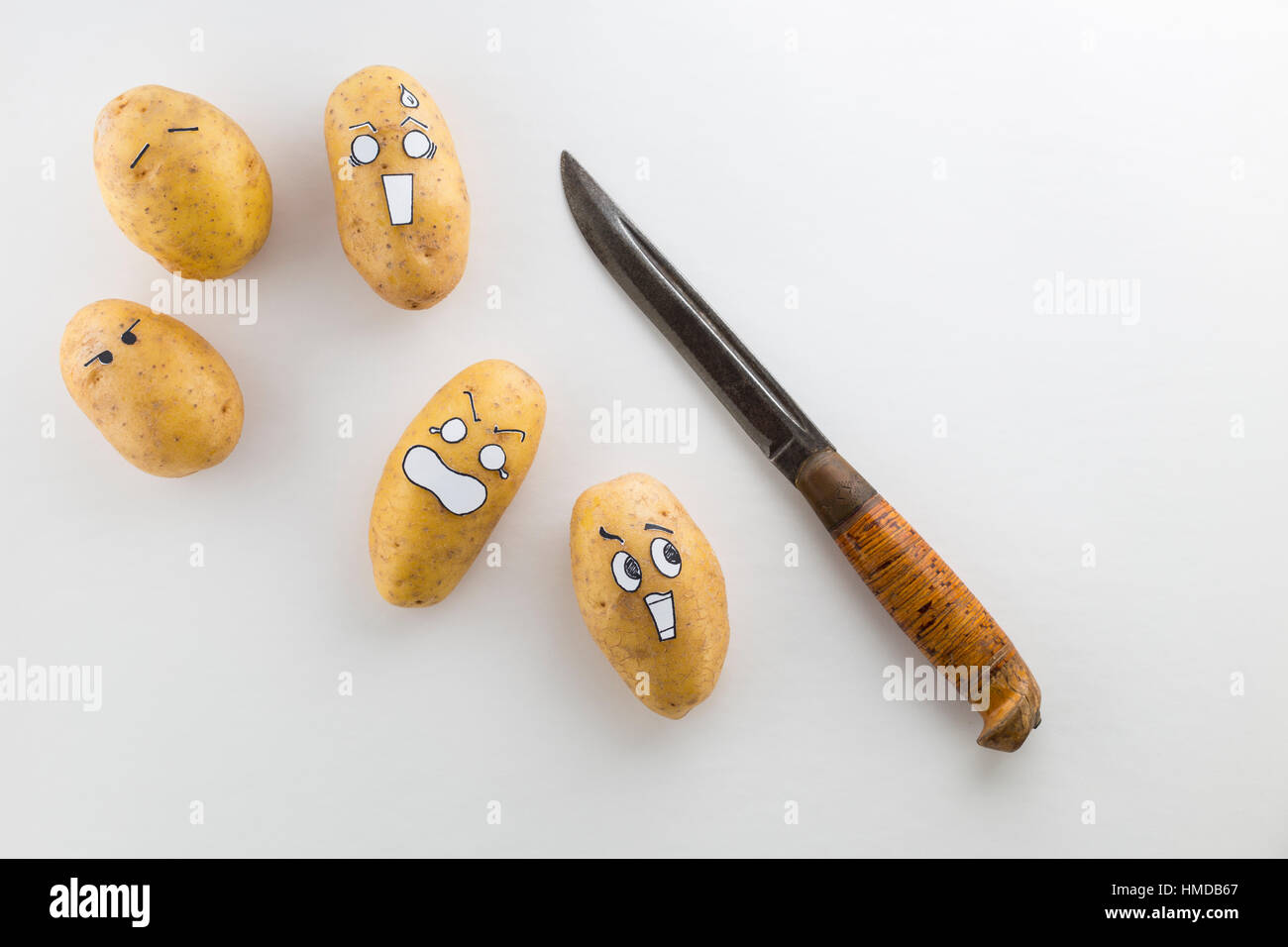 Frische Kartoffeln mit Cartoon Stil Gesichtern Verlegung auf weiße Fläche sind von einem Messer Angst. Stockfoto