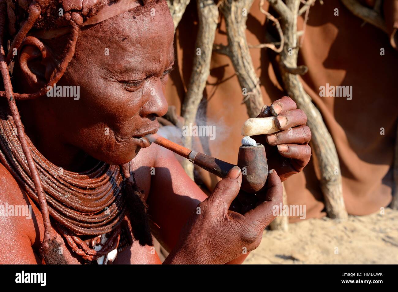 Himba Frau Beleuchtung und Rauchen ihr Rohr, Marienfluss Tal, Kaokoland Wüste, Namibia. Stockfoto