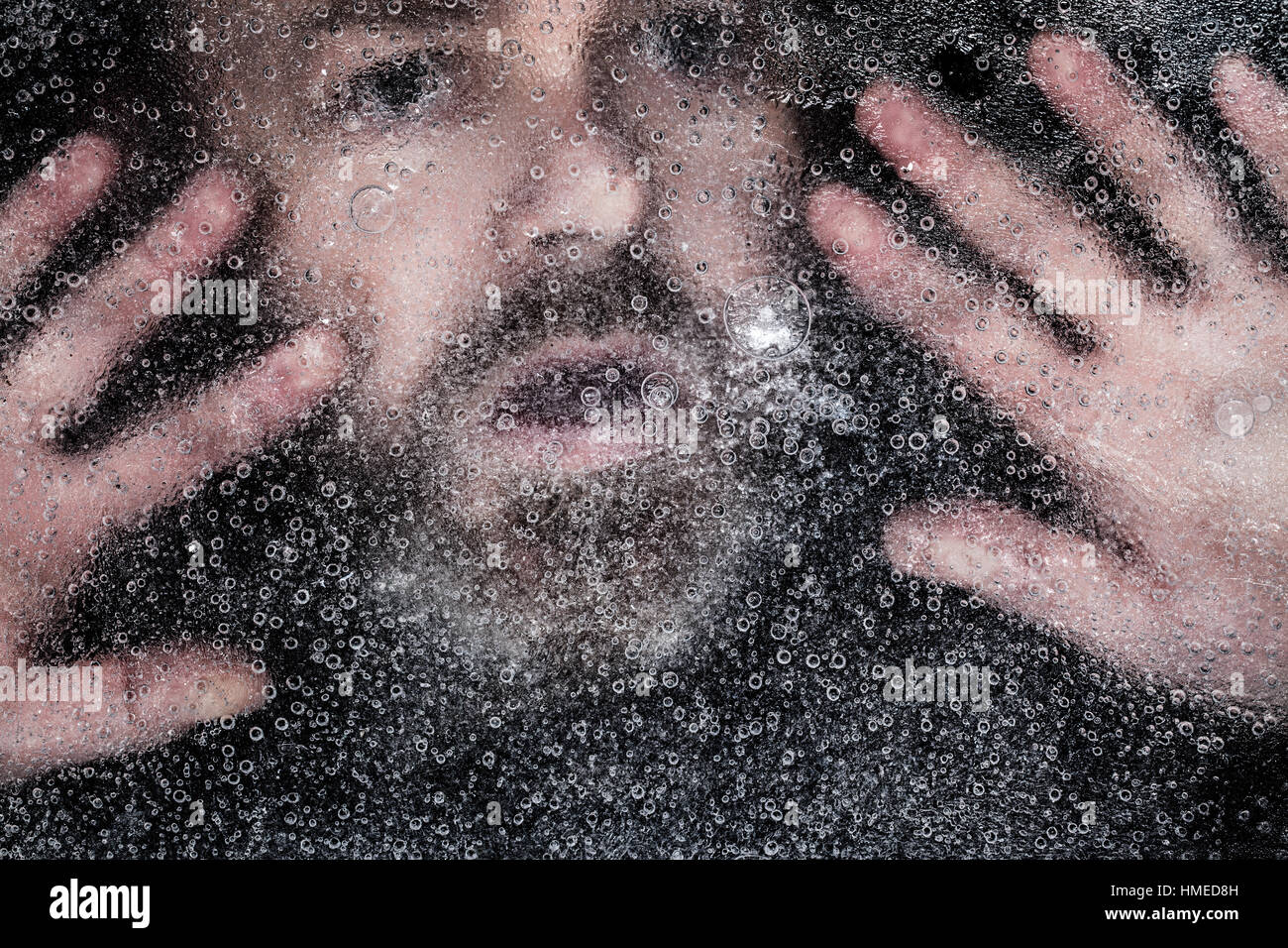 Angst Mann treibt auf dem Eis unter einem zugefrorenen See. Augen und Mund weit offen und mit einem dunklen Hintergrund ertrinken Stockfoto