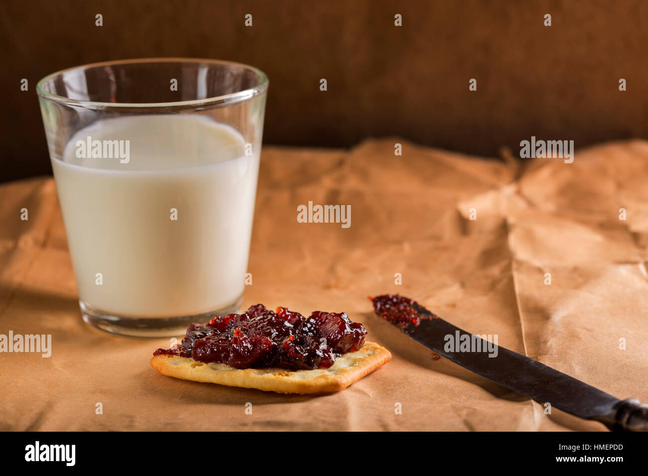 Ein Keks mit Marmelade und ein Glas gefüllt mit Milch im Hintergrund auf dem Papier Stockfoto