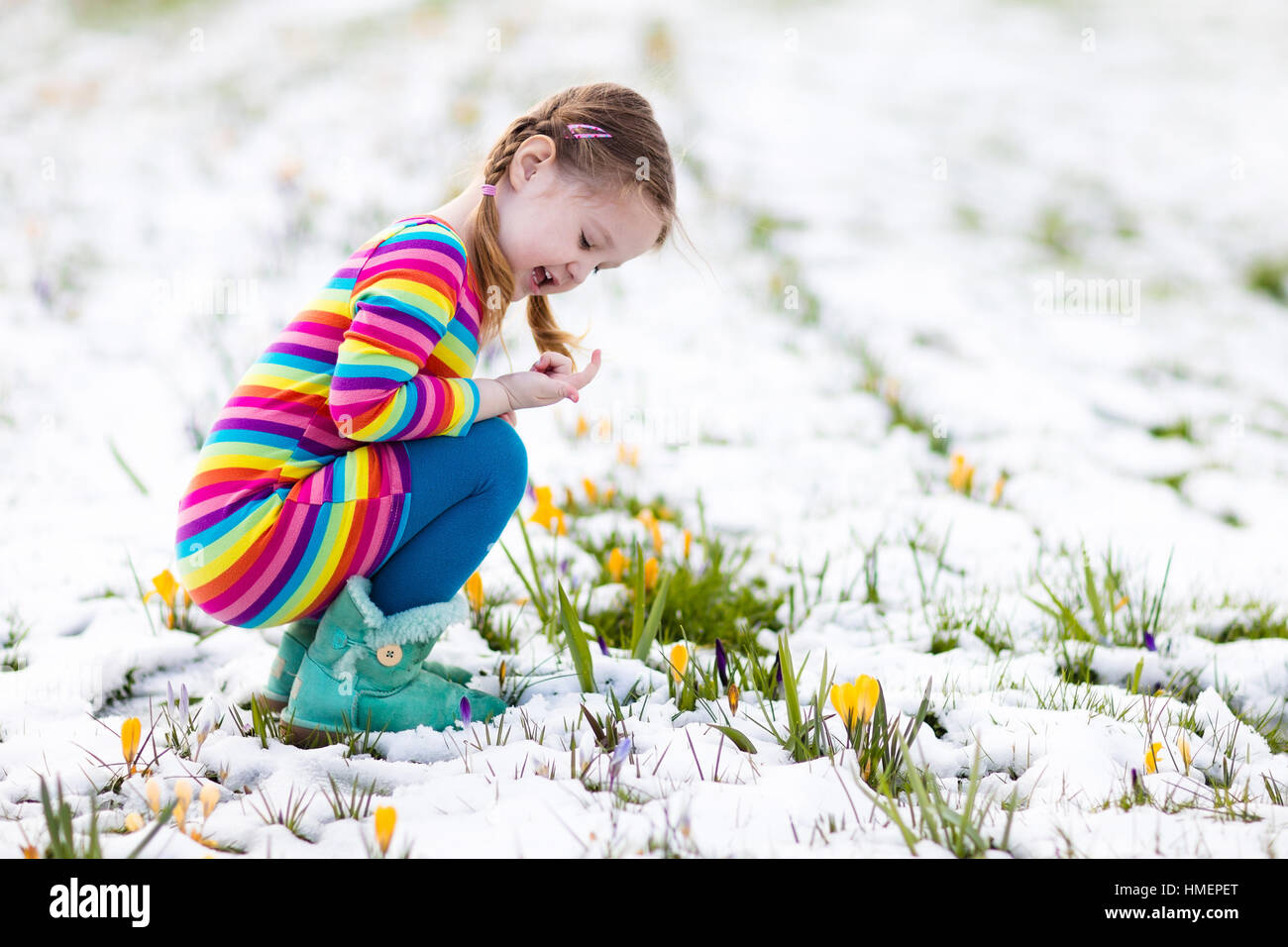Niedliche kleine Mädchen in buntes Kleid, die ersten Blumen im Frühling Crocus unter Schnee an kalten Tag beobachten. Kind Kommissionierung Garten Blume Stockfoto