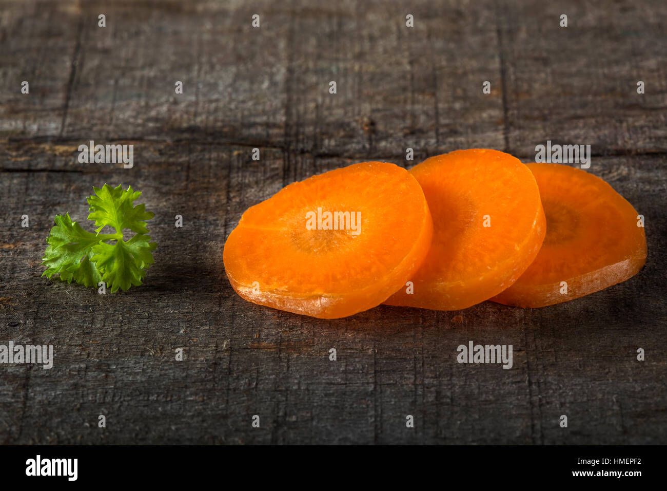Drei rohe Karotten Scheiben mit geschweiften Petersilie Blatt über alten rustikalen hölzernen Hintergrund Stockfoto