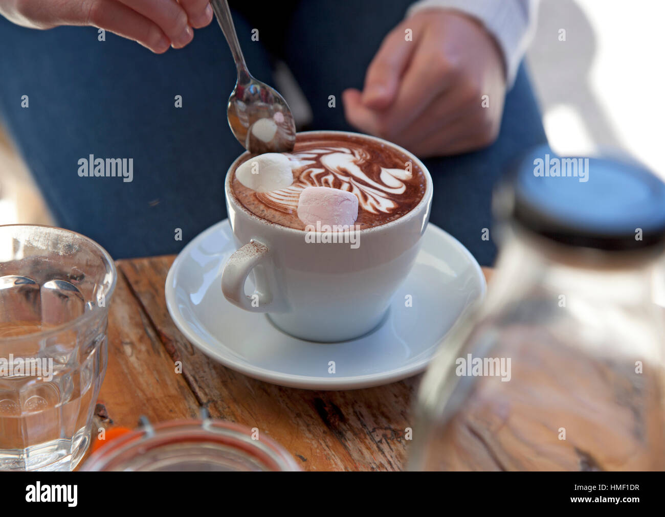 Ein junges Mädchen Löffel ihre heißen Schokolade mit Marshmallows auf einem rustikalen Cafétisch Stockfoto