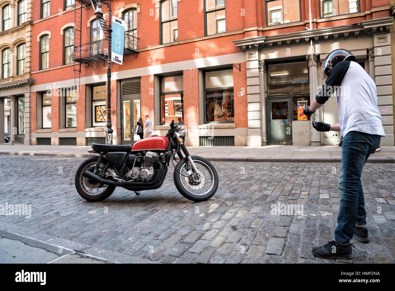 Soho, Manhattan, New York City, Mann, 20-30, in Reiten Fahrradhelm, stoping um sein Motorrad auf seinem Smartphone zu fotografieren. Stockfoto