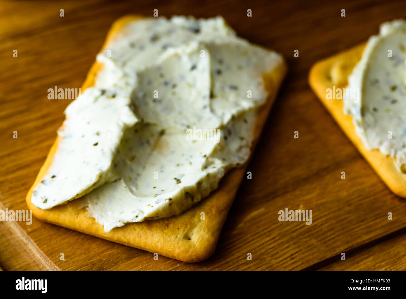 Cracker mit Kräuter Frischkäse bestreichen. Eine leckere und einfache Snack, hier auf einem Holztablett. Flachen Fokus und unscharfen Hintergrund. Stockfoto