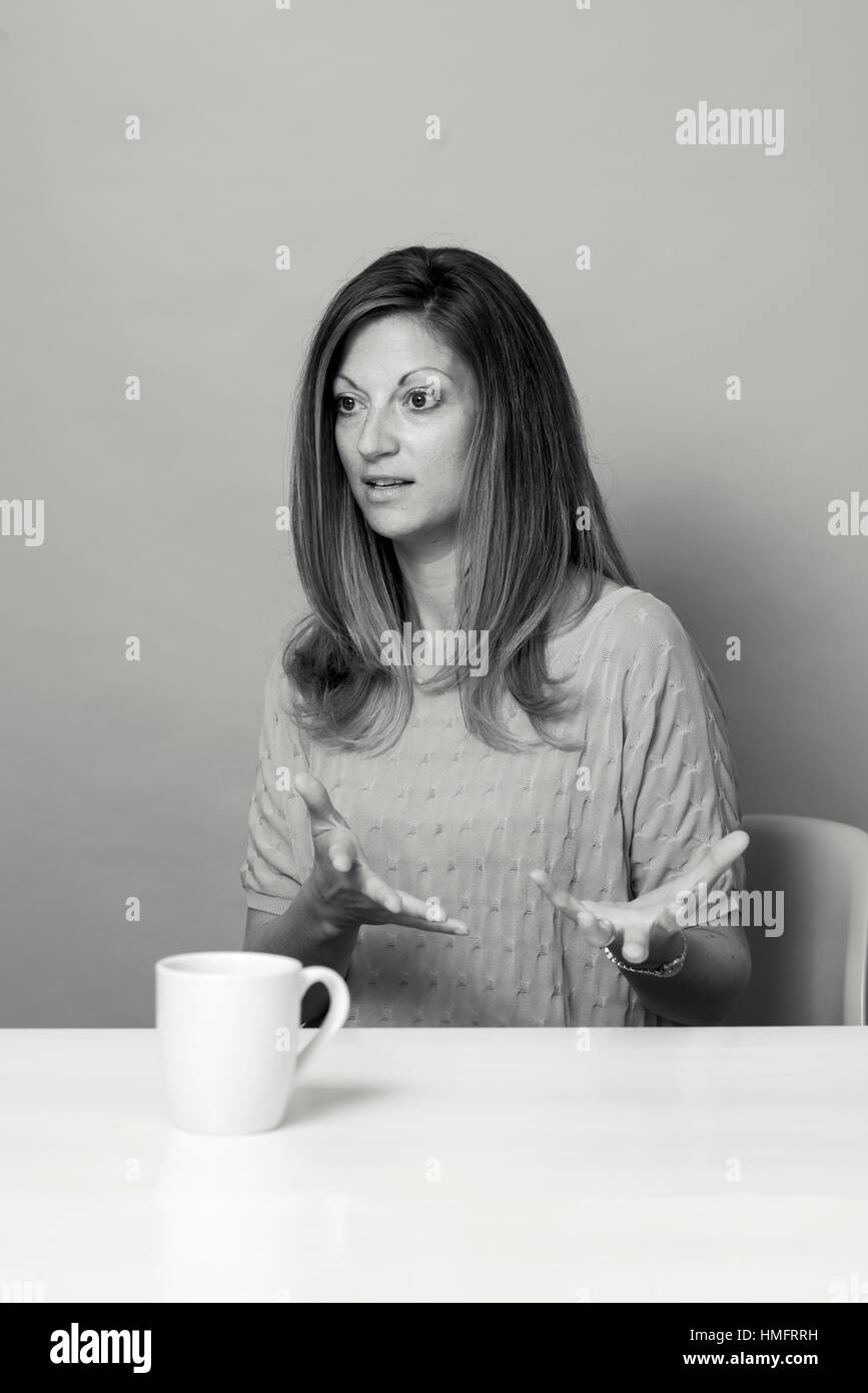 Ein junger Junge weiße Frau sitzt an einem Tisch, trinken eine Tasse Kaffee, während gestikulierend und sprechen über ein Thema und suchen gerne Stockfoto