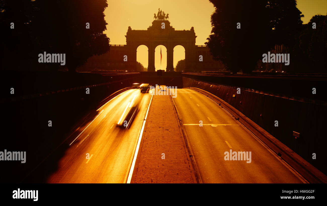 Brüsseler Jubelpark Tunnel am Morgen. Autos fahren vor dem Wahrzeichen Triumphbogen Denkmal und die Nationalflagge von Belgien Stockfoto