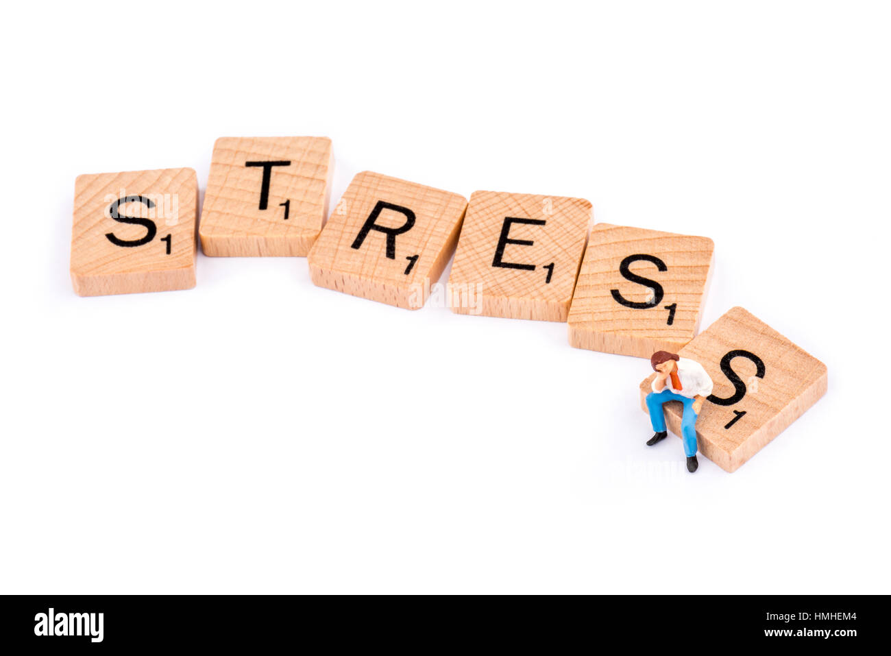 Scrabble Buchstaben bilden das Wort STRESS. Ein junger Mann sitzt allein auf den Buchstaben S. Stockfoto