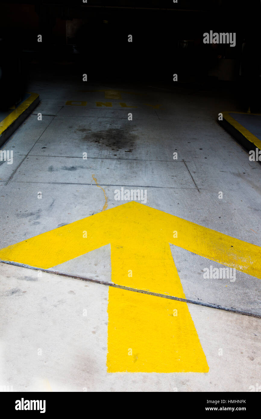 Gelber Pfeil auf Bürgersteig vor Dunkelheit Stockfoto