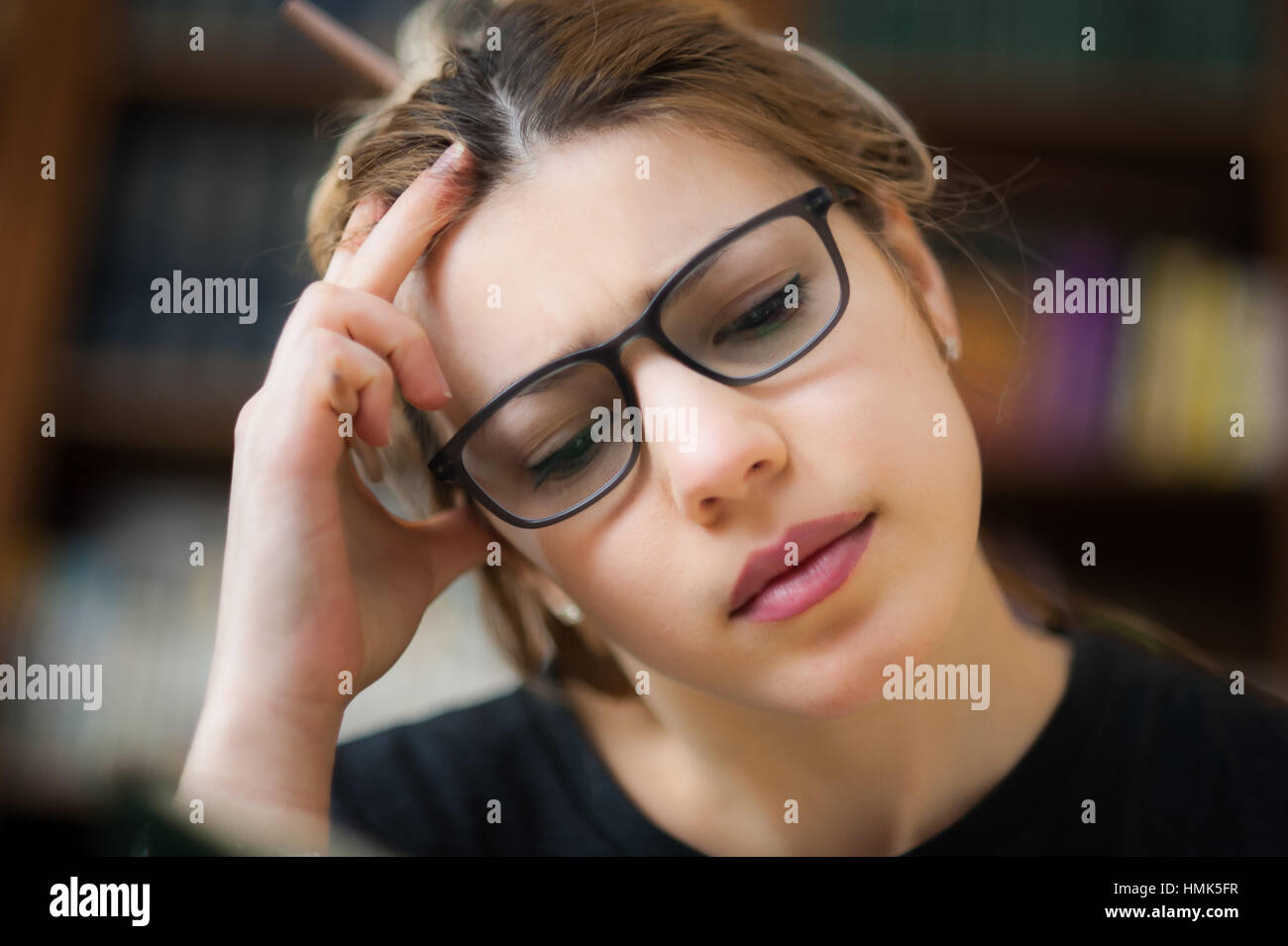 Junge Studentin in Bibliothek, Porträt während konzentriert studieren, aus Fokus Bücherregal im Hintergrund Stockfoto