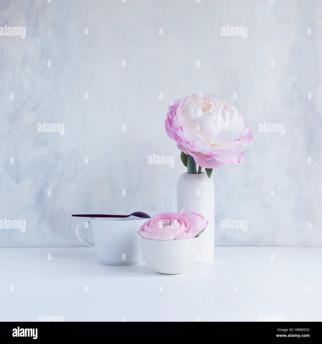 Stillleben mit rosa Ranunkeln in weiße Keramikschale und rosa Pfingstrose in weiße kleine Keramik-Vase mit Becher und Löffel Stockfoto