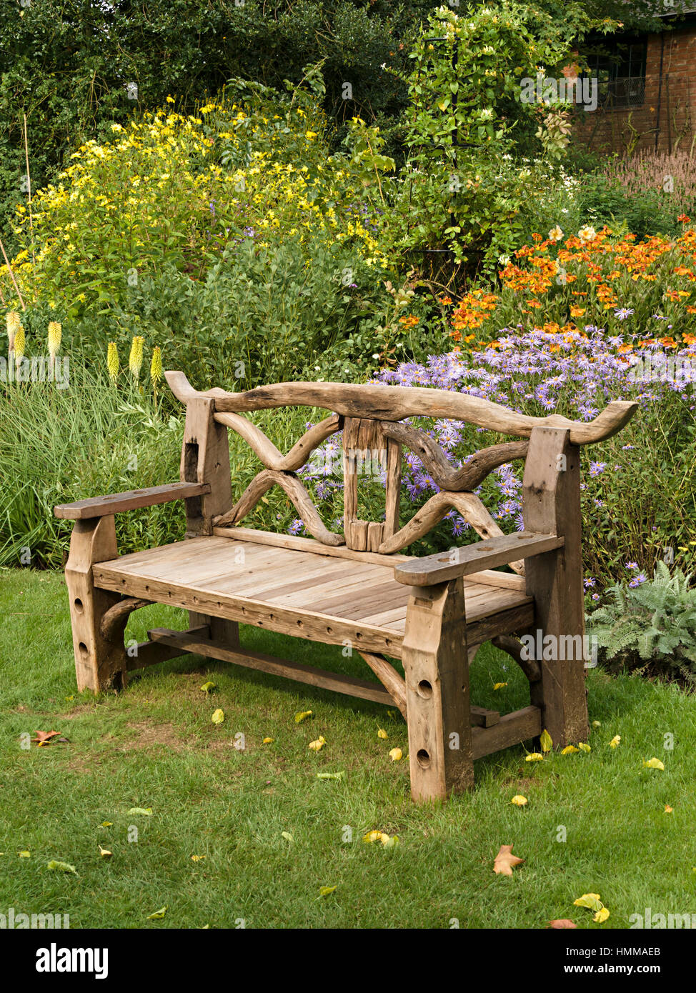 Kunstvolle, rustikal, hölzerne Garten Sitzbank, hergestellt aus recycelten Holzteile vor unteren Betten, Coton Manor Gardens, Northamptonshire, England, UK Stockfoto