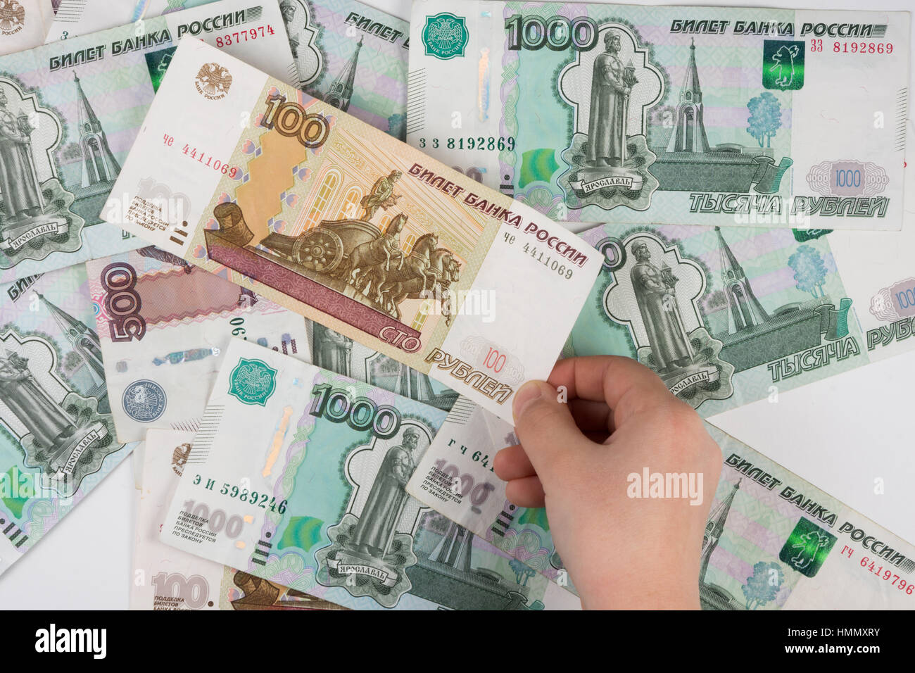 Hand für Kinder nimmt die Bezeichnung aus dem Haufen von zufällig verstreute russische Banknoten unterschiedlicher Konfession Stockfoto