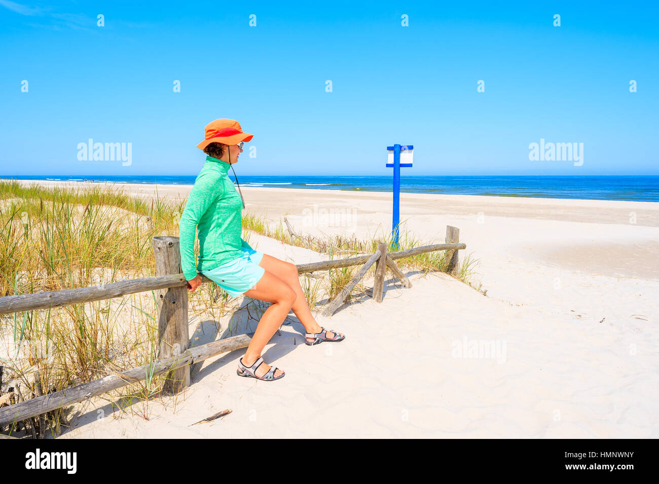 Junge Frau sitzt auf Holzzaun und Blick auf den wunderschönen weißen Sandstrand, Ostsee, Polen Stockfoto