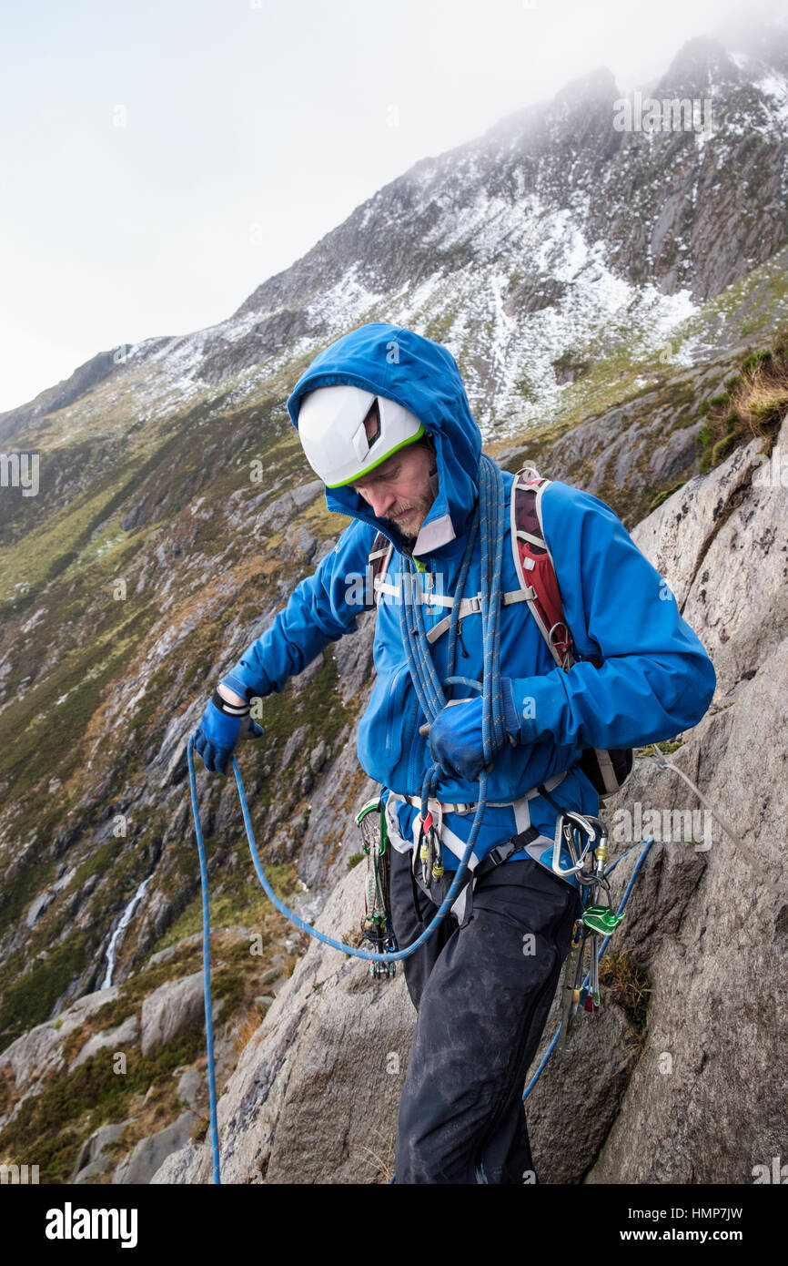 Ein Kletterer, wickeln ein Kletterseil um seinen Körper bereitet sich eine Gerangel in Cwm Idwal, Ogwen, Snowdonia, North Wales, UK, Großbritannien führen. Stockfoto
