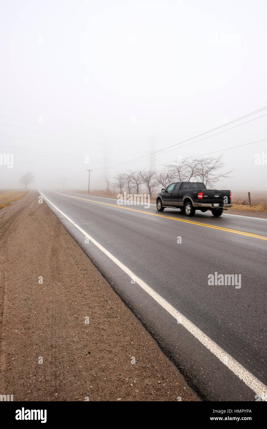 Ein schwarzen Pickup-Truck fährt auf eine asphaltierte Landstraße in einem nebligen Morgen in Südwest-Ontario, Kanada. Stockfoto