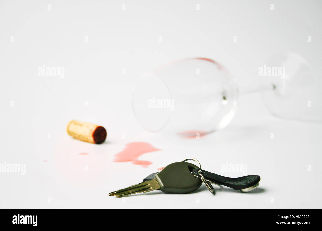Autoschlüssel auf weiße Fläche liegen. Gefallenen Weinglas mit verschüttetem Rotwein und Kork im Hintergrund. Konzept für keine Trunkenheit am Steuer Stockfoto