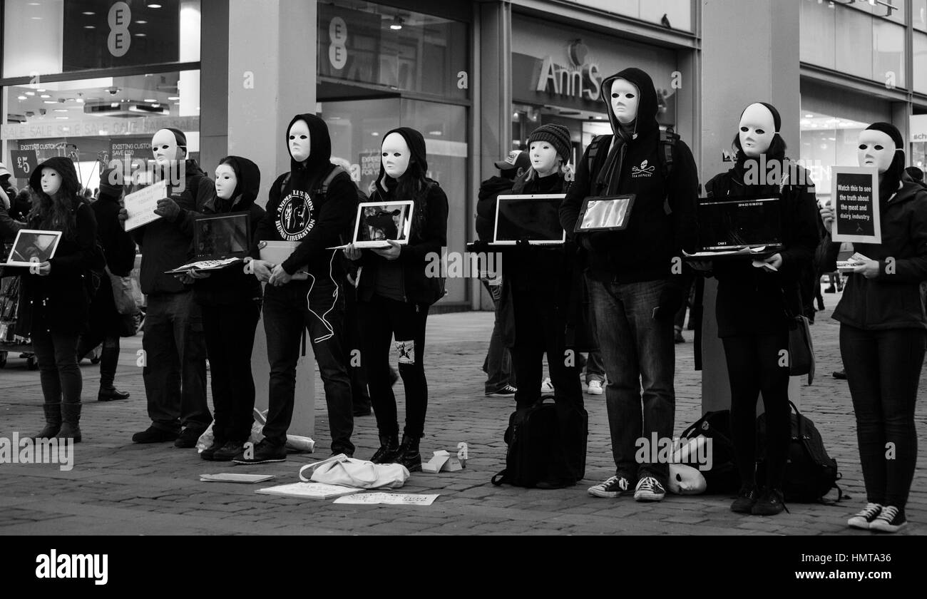 Demonstranten mit einfachen Masken, alle in schwarz gekleidet, in der Fußgängerzone der Innenstadt oder Stadt Zentrum. Stockfoto