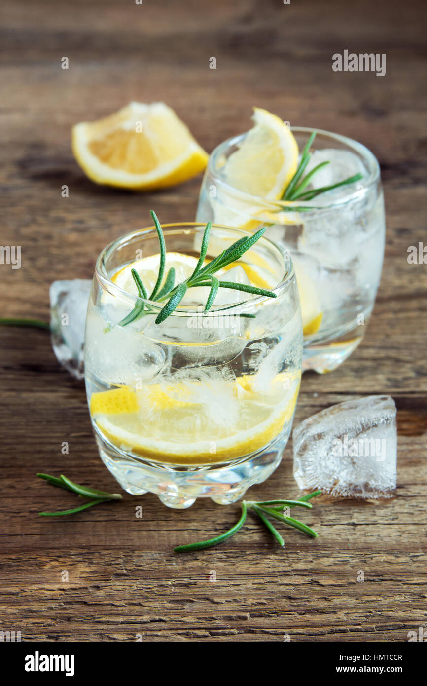Alkoholische Getränke (Gin Tonic Cocktail) mit Zitrone, Rosmarin und Eis am rustikalen Holztisch, Textfreiraum Stockfoto