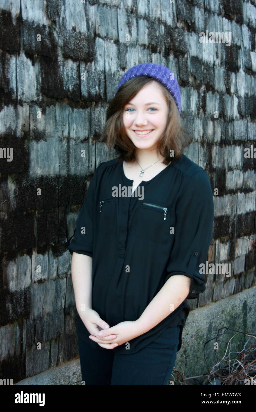 Braunen Haaren, blauen Augen Teen in lila Hut stehen neben dem Strumpf Schindeln Wand. Stockfoto