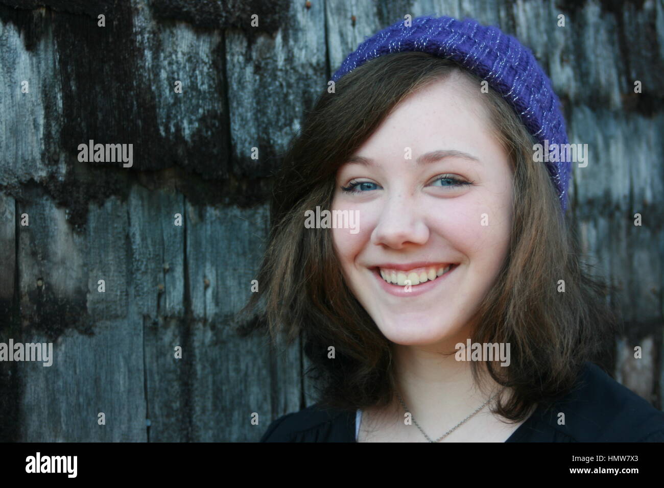 Braunen Haaren, blauen Augen Teen in lila Hut stehen neben dem Strumpf Schindeln Wand. Stockfoto
