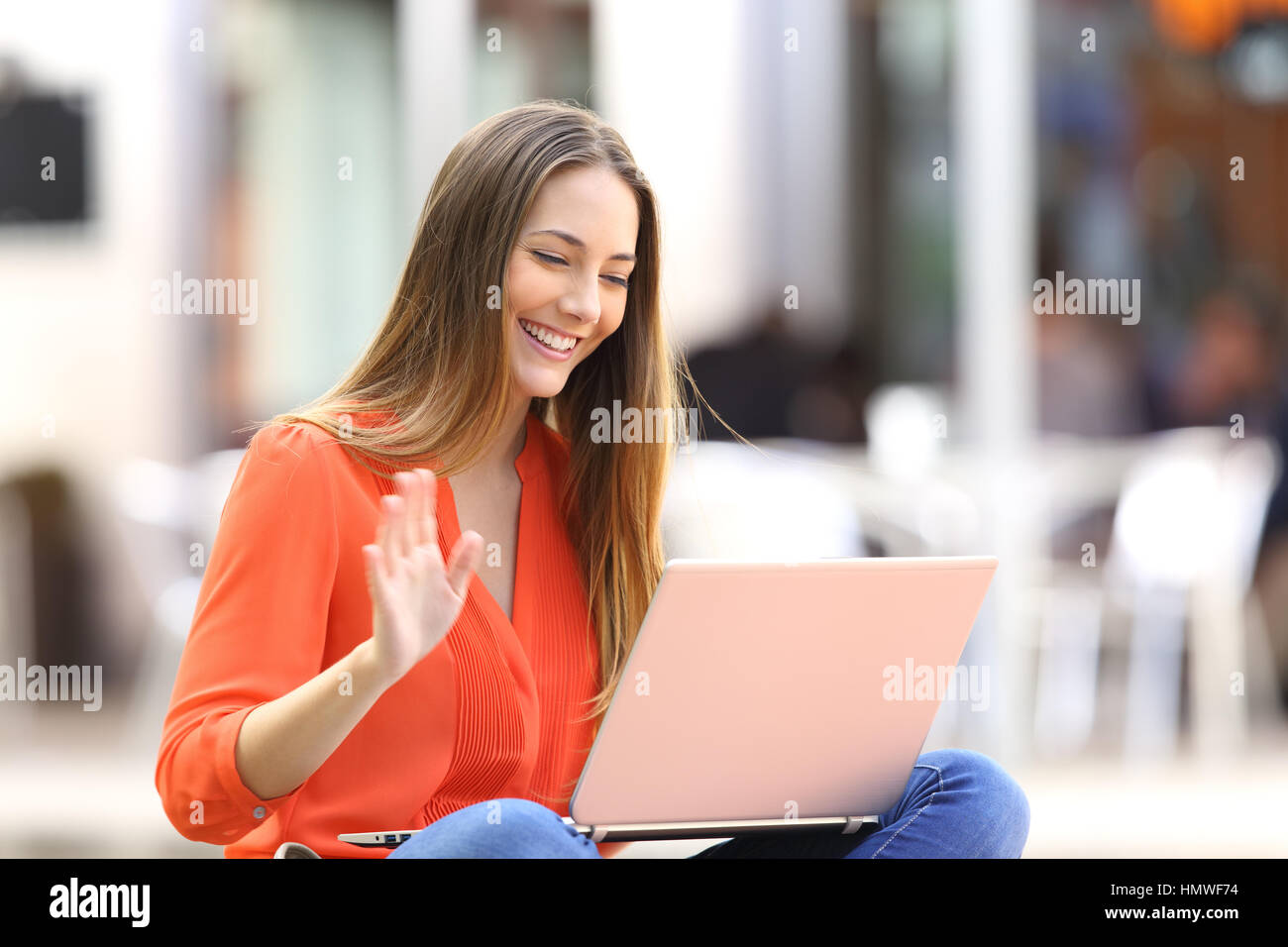 Glückliche Frau am Linie in einer Videokonferenz mit einem Laptop sitzen auf einer Bank in der Straße Stockfoto