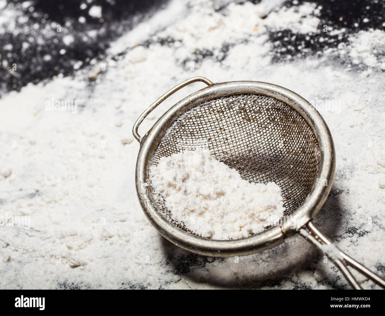 Metall-Sieb mit Mehl auf einem schwarzen Hintergrund zu verschütten. Stockfoto